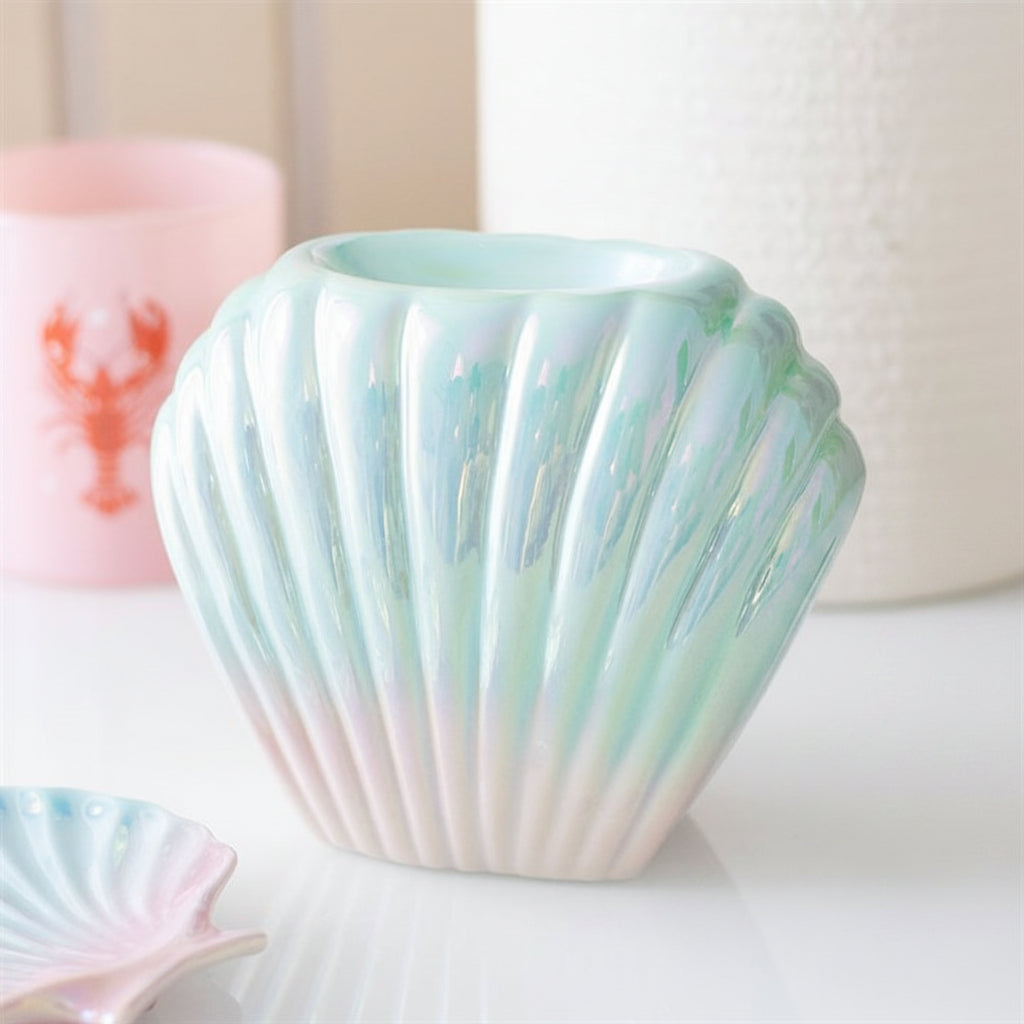 Iridescent shell-shaped candle holder on a white surface with a blurred background